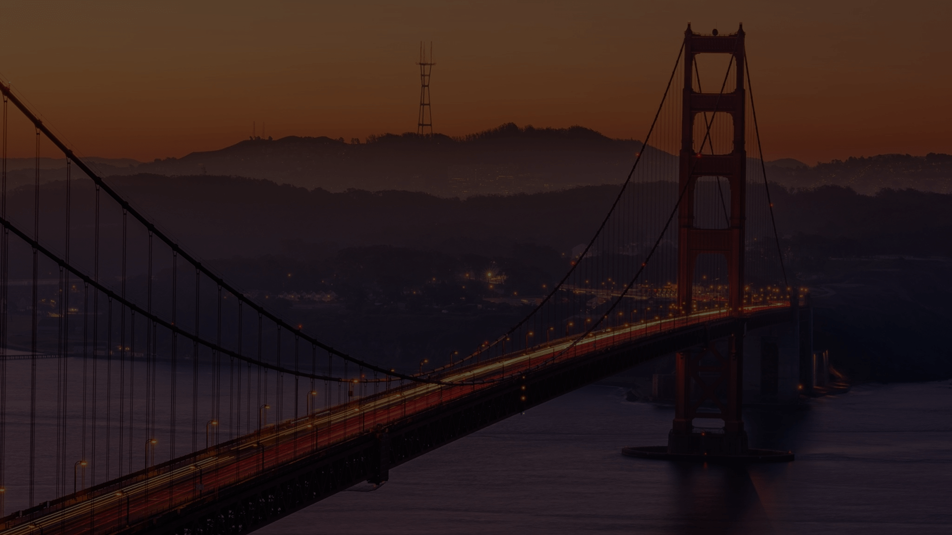 Golden Gate Bridge at dusk with light trails from cars and hills in the background.